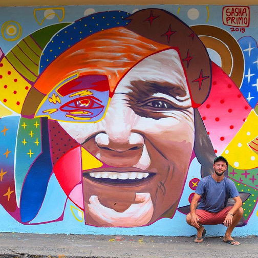A man squats in front of a mural