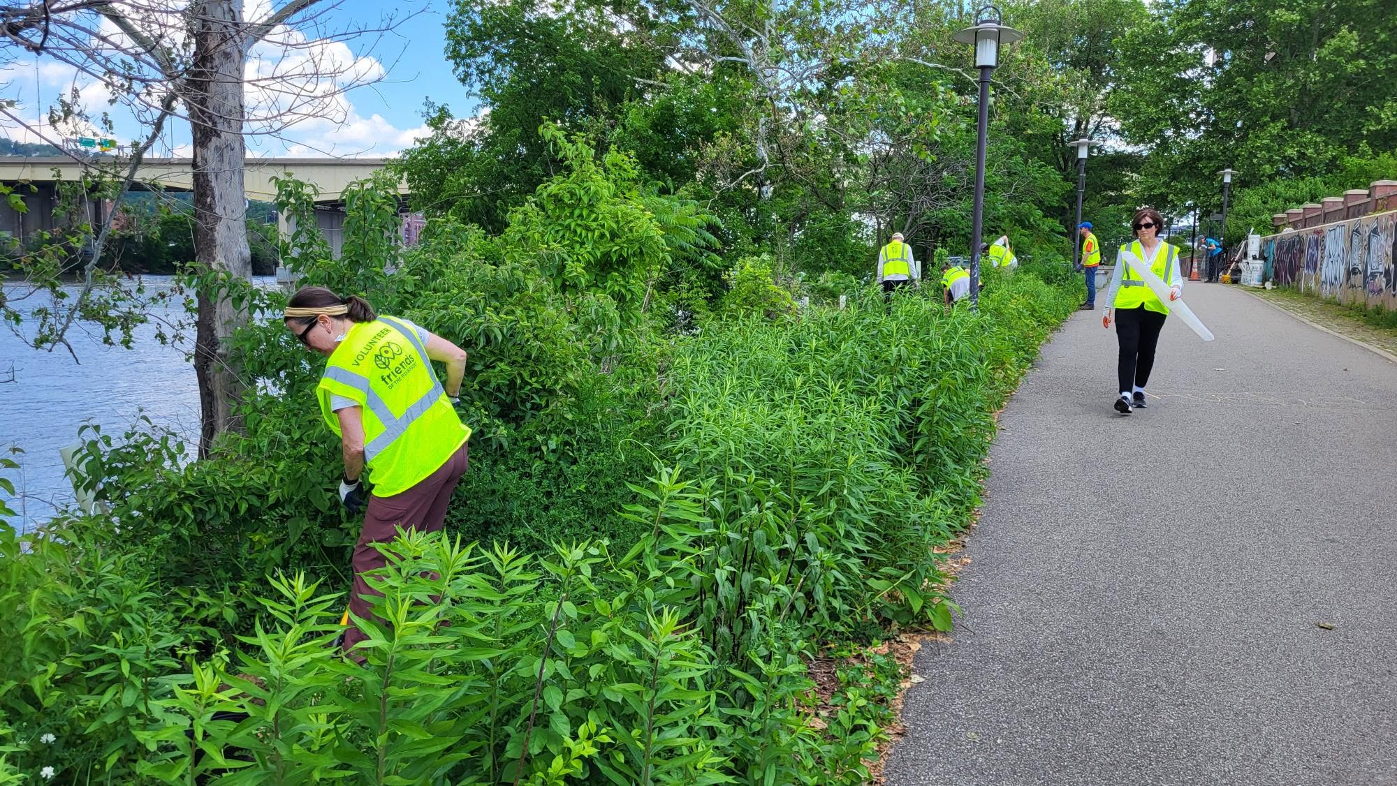 A group of people in yellow vests clean up a river side walk.