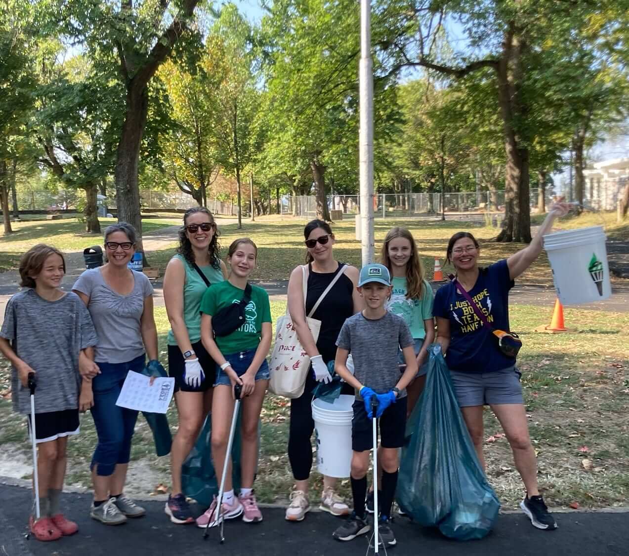 A group of people gather for a photo in the park holding their litter clean-up gear