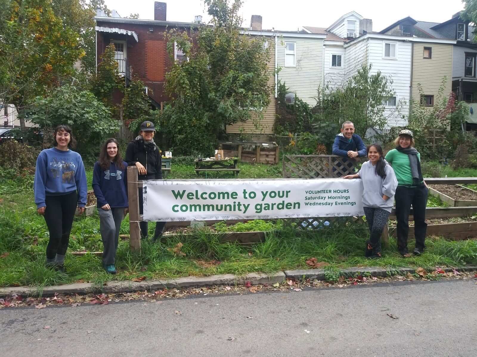 Six people group around a sign that reads: Welcome to your community garden